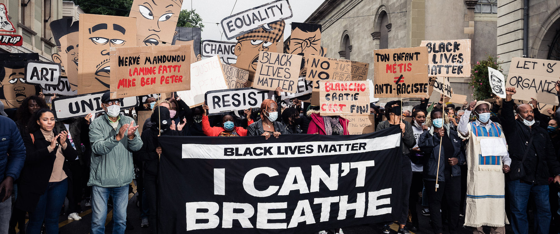 On the image you see many people holding sign like "Black lives matter", "Equality", "Blanchocratie c'est fini" and others. There is a big black banner with white text written "Black lives matter, I can't breath".