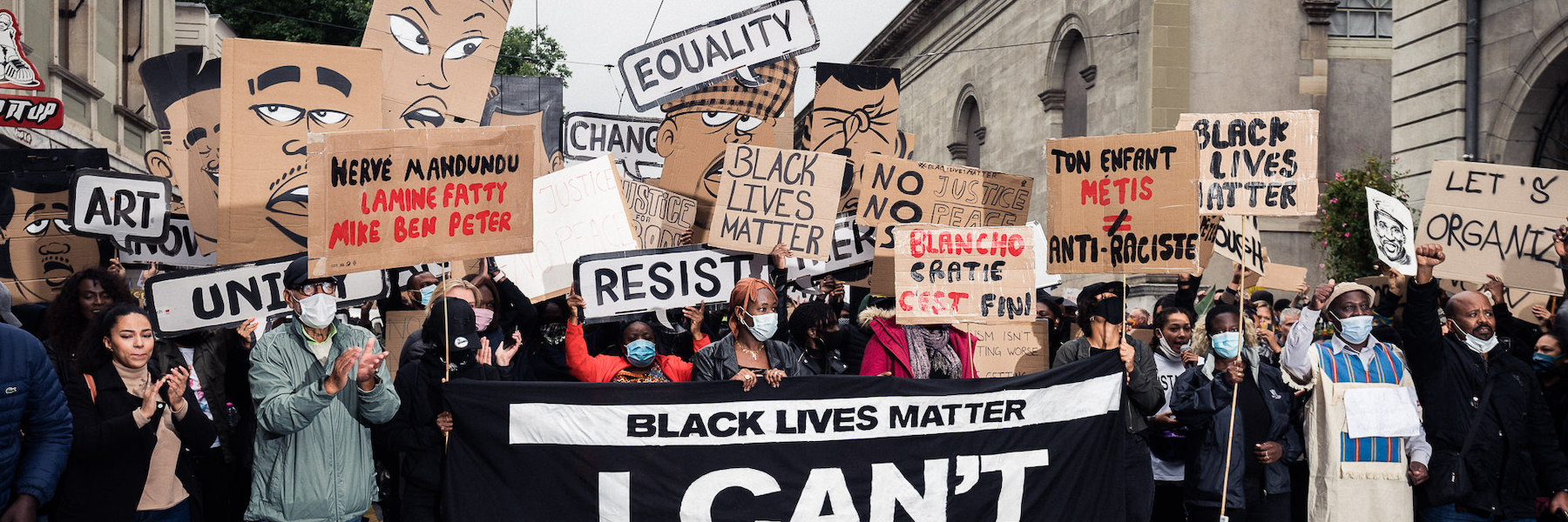 On the image you see many people holding sign like "Black lives matter", "Equality", "Blanchocratie c'est fini" and others. There is a big black banner with white text written "Black lives matter, I can't breath".